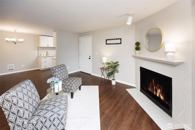 living room featuring visible vents, baseboards, dark wood-style flooring, and a tile fireplace