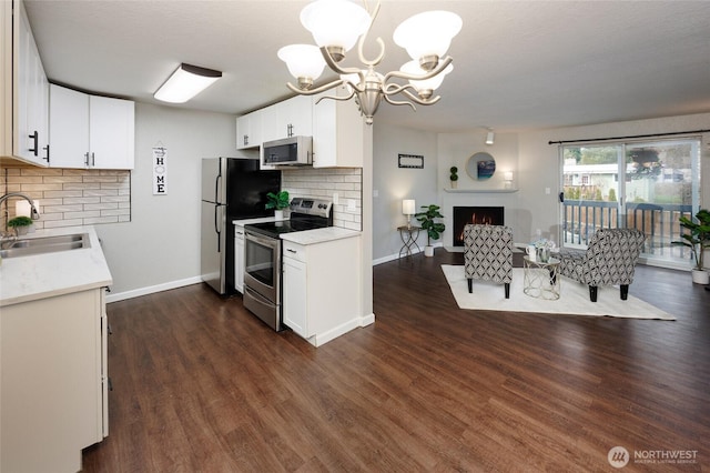 kitchen with a sink, dark wood-style floors, open floor plan, a lit fireplace, and appliances with stainless steel finishes