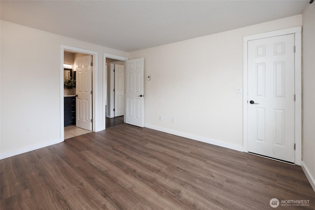 unfurnished bedroom with ensuite bath, wood finished floors, and baseboards