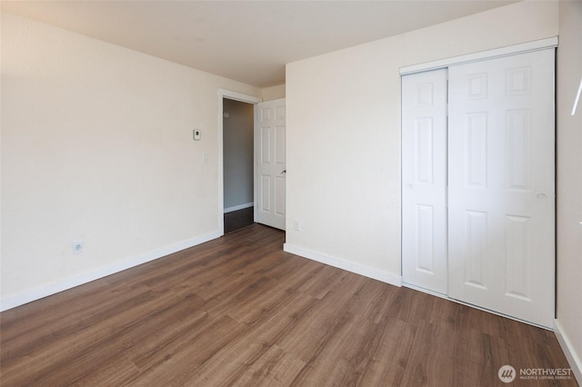 unfurnished bedroom featuring wood finished floors, baseboards, and a closet