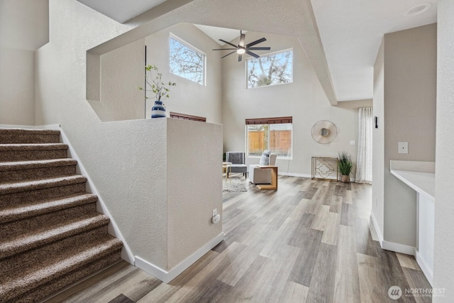 stairway featuring a fireplace, wood finished floors, baseboards, and a towering ceiling