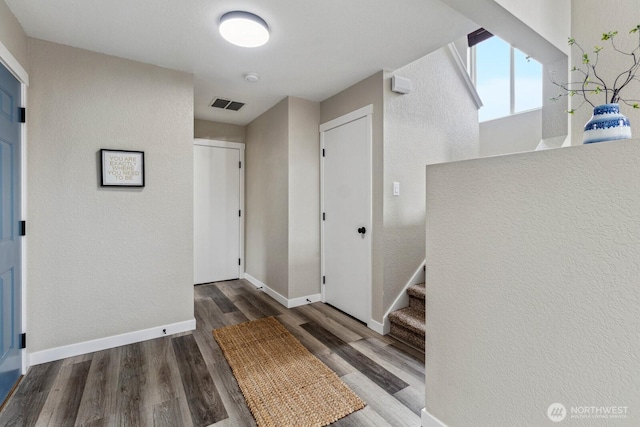 hallway featuring wood finished floors, visible vents, baseboards, stairs, and a textured wall