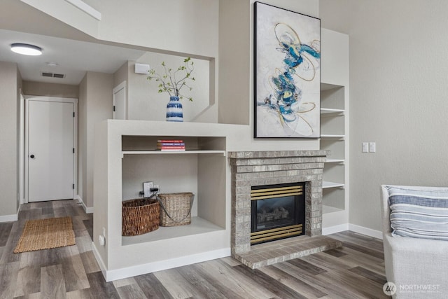 living room with built in features, wood finished floors, visible vents, baseboards, and a brick fireplace