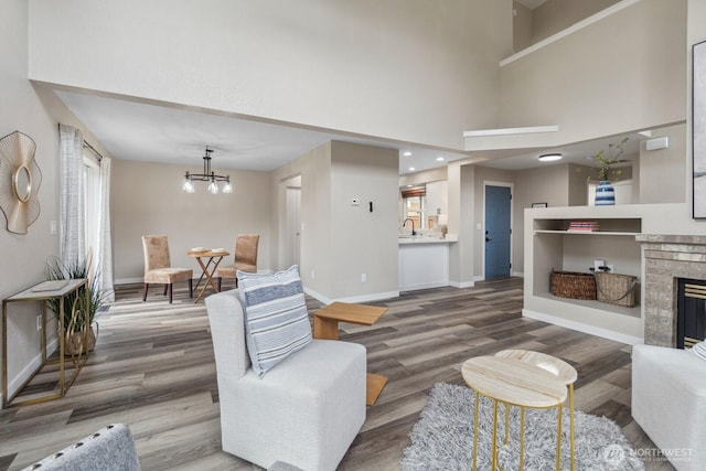 living room with a notable chandelier, a brick fireplace, baseboards, and wood finished floors