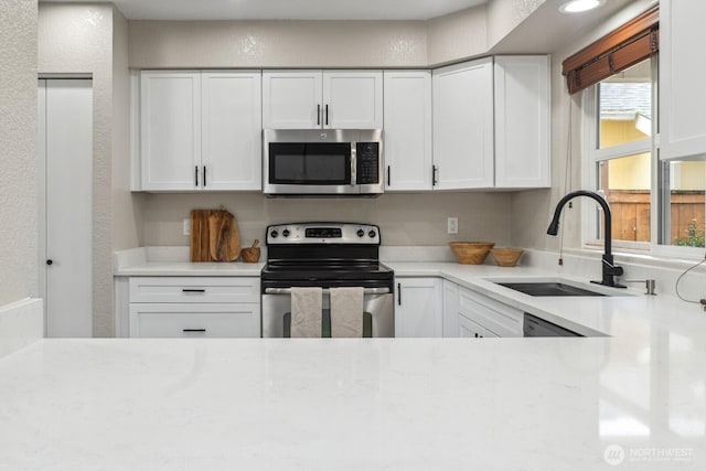 kitchen featuring white cabinetry, stainless steel appliances, a textured wall, and a sink