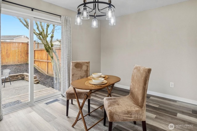 dining area with visible vents, wood finished floors, baseboards, and a chandelier