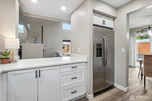 kitchen with light countertops, a textured wall, stainless steel refrigerator with ice dispenser, wood finished floors, and white cabinets