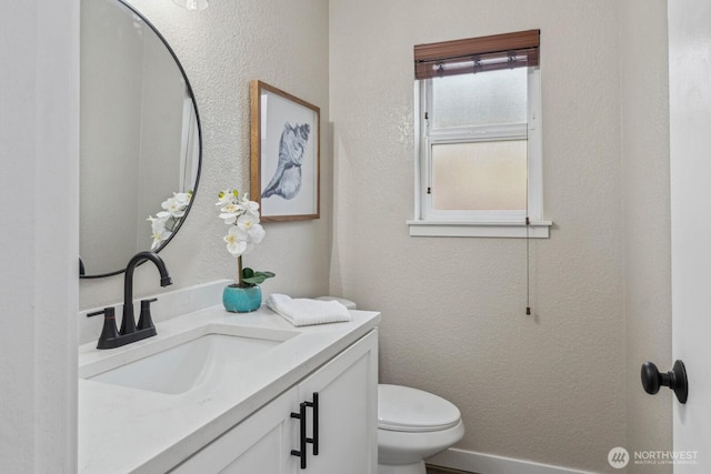 bathroom featuring vanity, toilet, a textured wall, and baseboards