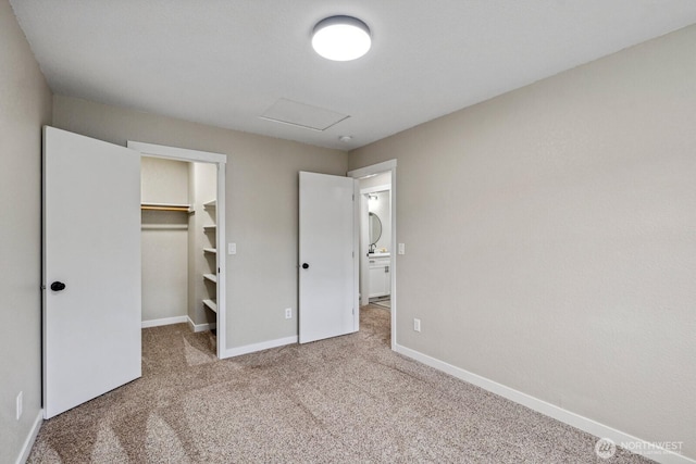 unfurnished bedroom featuring a walk in closet, a closet, carpet floors, baseboards, and attic access