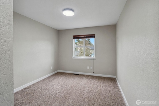 spare room with baseboards, carpet floors, visible vents, and a textured wall