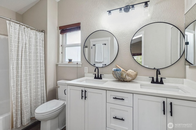 full bath featuring a sink, toilet, double vanity, and a textured wall