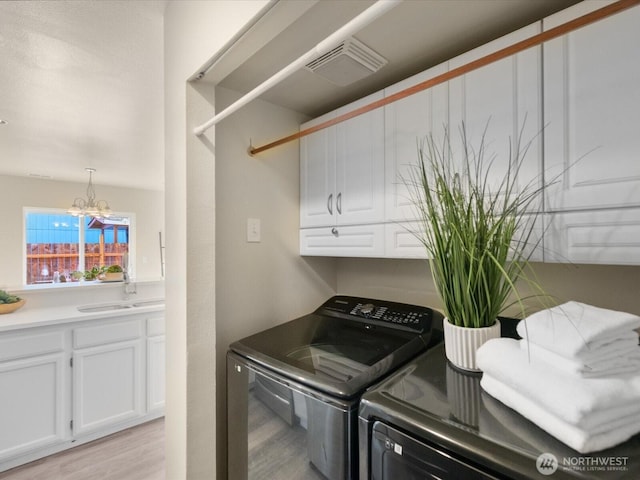 laundry room featuring visible vents, a notable chandelier, a sink, washing machine and dryer, and light wood finished floors