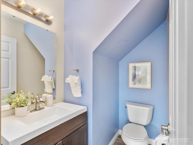 half bath featuring vanity, lofted ceiling, toilet, and baseboards