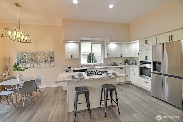 kitchen featuring a sink, a kitchen breakfast bar, a center island, appliances with stainless steel finishes, and white cabinets