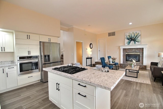 kitchen featuring visible vents, open floor plan, appliances with stainless steel finishes, wood finished floors, and white cabinets