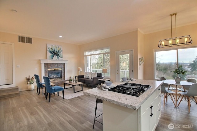 kitchen with visible vents, light wood-style flooring, black gas cooktop, white cabinetry, and a tile fireplace