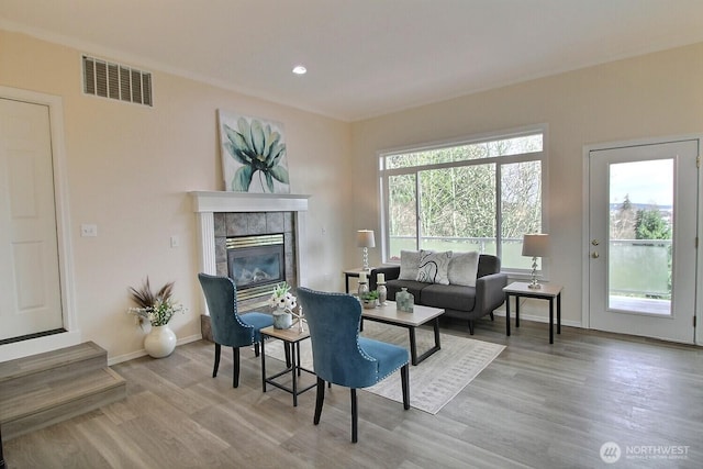 living room with a tiled fireplace, visible vents, baseboards, and wood finished floors