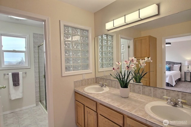 ensuite bathroom featuring double vanity, a stall shower, and a sink