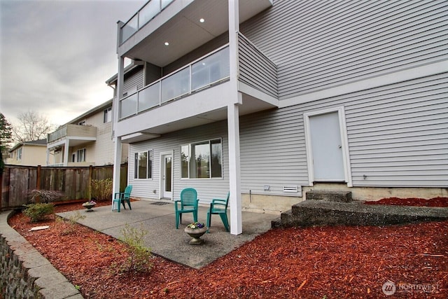 back of property featuring a balcony, entry steps, a patio, and fence