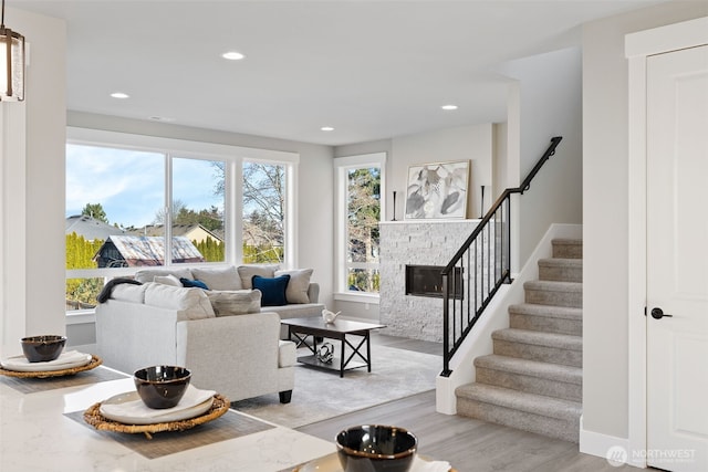 living area with recessed lighting, light wood-style floors, a stone fireplace, baseboards, and stairs