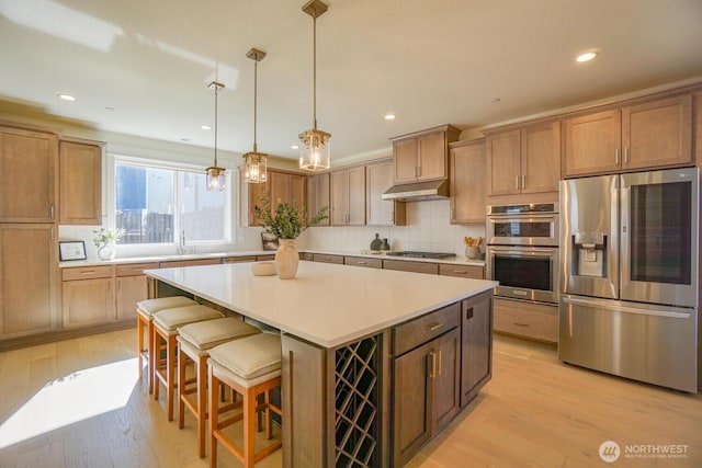 kitchen featuring under cabinet range hood, appliances with stainless steel finishes, a center island, and light wood-type flooring