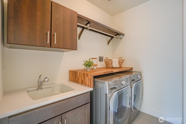 washroom with washing machine and clothes dryer, cabinet space, baseboards, and a sink