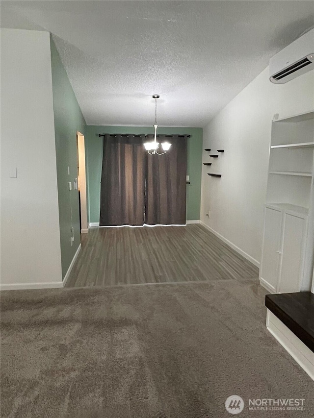 interior space with a textured ceiling, carpet flooring, baseboards, and a wall mounted AC