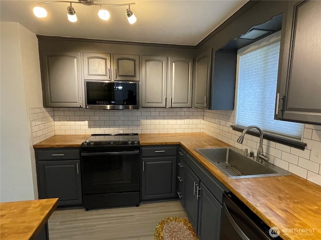 kitchen with wooden counters, light wood-style flooring, a sink, black appliances, and tasteful backsplash