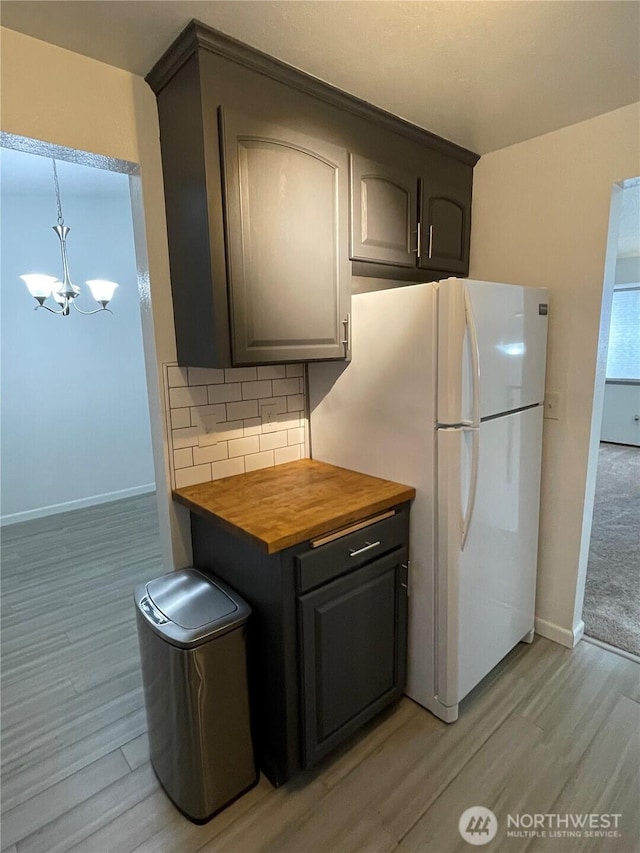 kitchen featuring baseboards, light wood finished floors, freestanding refrigerator, wood counters, and backsplash