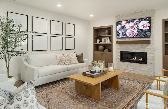 living area with built in features, wood finished floors, recessed lighting, a stone fireplace, and baseboards