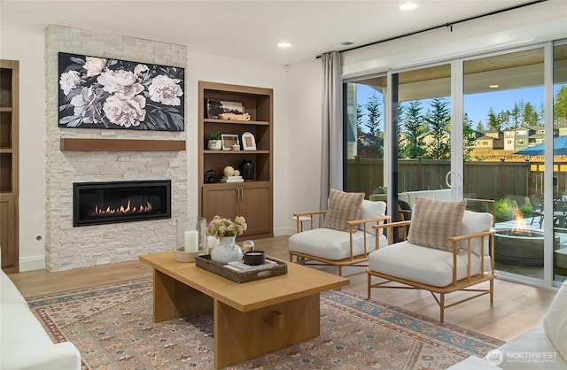 living area with recessed lighting, built in shelves, a stone fireplace, and wood finished floors