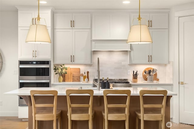 kitchen featuring a kitchen bar, backsplash, hanging light fixtures, and light countertops