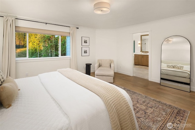 bedroom with baseboards, ensuite bath, wood finished floors, and crown molding