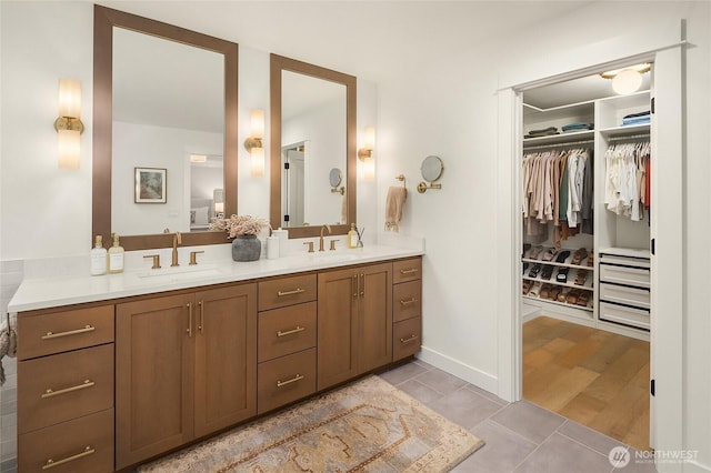 full bathroom with a walk in closet, double vanity, baseboards, and a sink