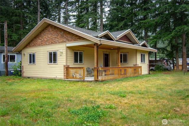 back of house featuring a yard, stone siding, and a shingled roof