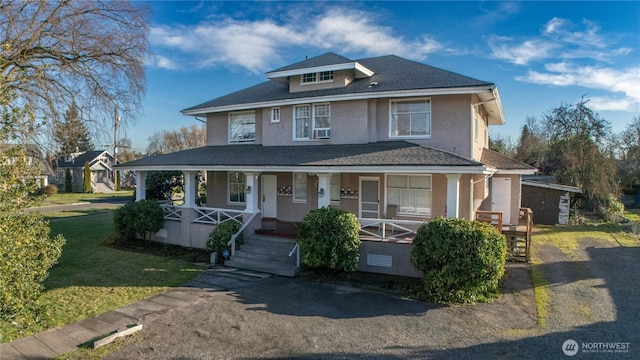 american foursquare style home with a front lawn, stucco siding, covered porch, and a shingled roof