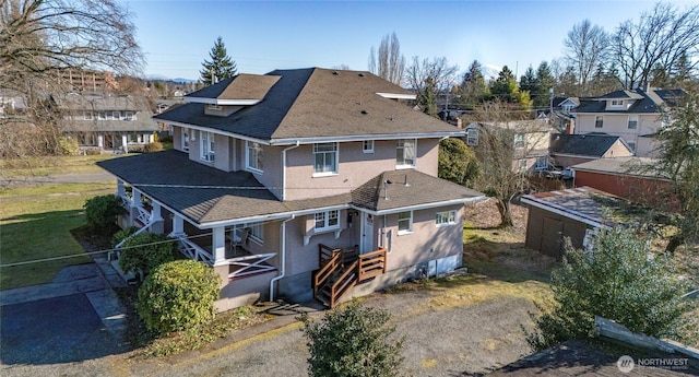 rear view of property with stucco siding, driveway, and roof with shingles