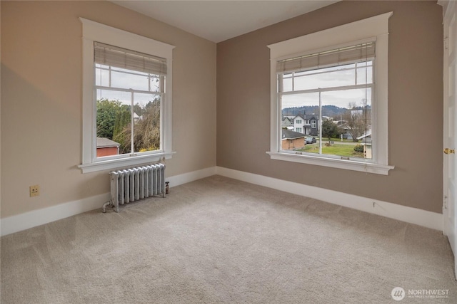 carpeted spare room featuring radiator heating unit, baseboards, and plenty of natural light