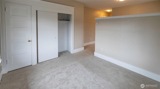 unfurnished bedroom featuring baseboards, a closet, and light carpet