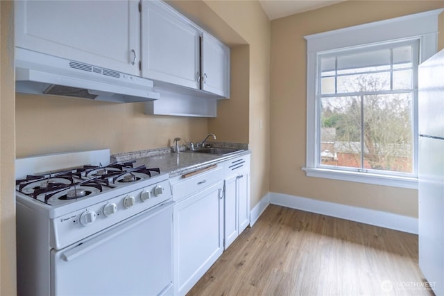 kitchen featuring white gas stove, under cabinet range hood, freestanding refrigerator, white cabinets, and baseboards