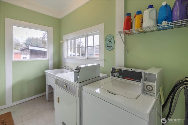 laundry area featuring washing machine and clothes dryer, light tile patterned floors, a wealth of natural light, and a sink