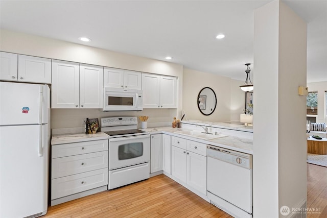 kitchen with white appliances, white cabinets, light wood-type flooring, and a sink