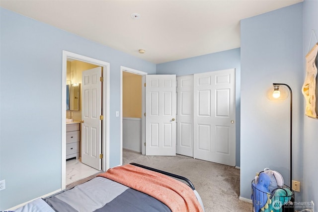 bedroom featuring a closet, connected bathroom, baseboards, and carpet