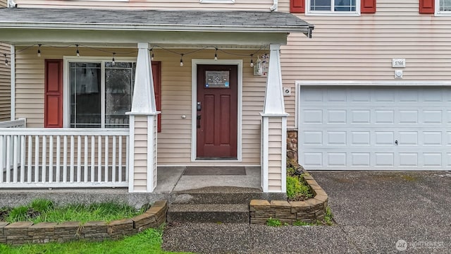 view of exterior entry with a garage, a porch, and a shingled roof