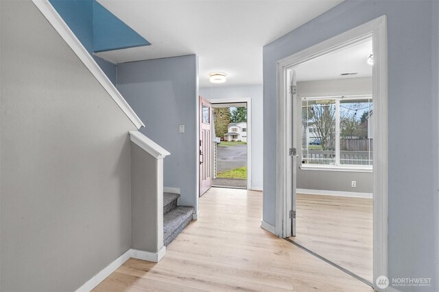 foyer featuring baseboards, light wood-style flooring, and stairs