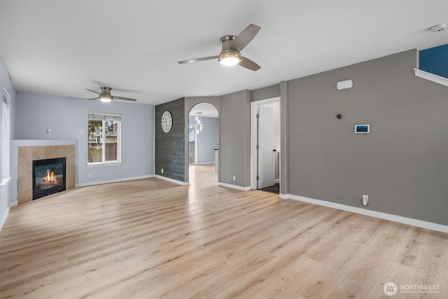 unfurnished living room featuring ceiling fan, baseboards, light wood-type flooring, a fireplace, and arched walkways