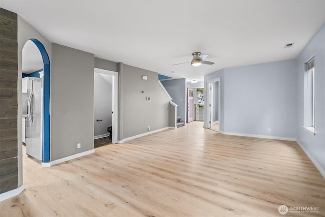 unfurnished living room with arched walkways, ceiling fan, baseboards, and light wood-style floors