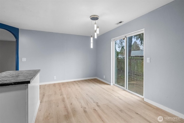 unfurnished dining area featuring baseboards, arched walkways, visible vents, and light wood-style flooring