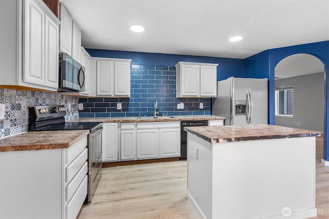 kitchen with light wood finished floors, a sink, stainless steel appliances, white cabinets, and a center island