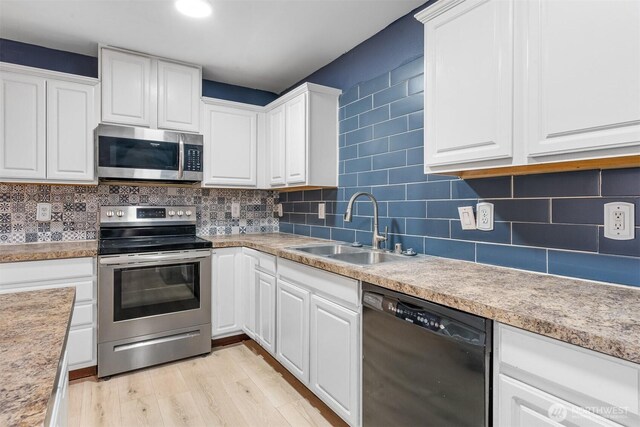 kitchen with a sink, backsplash, light wood-style floors, appliances with stainless steel finishes, and white cabinets